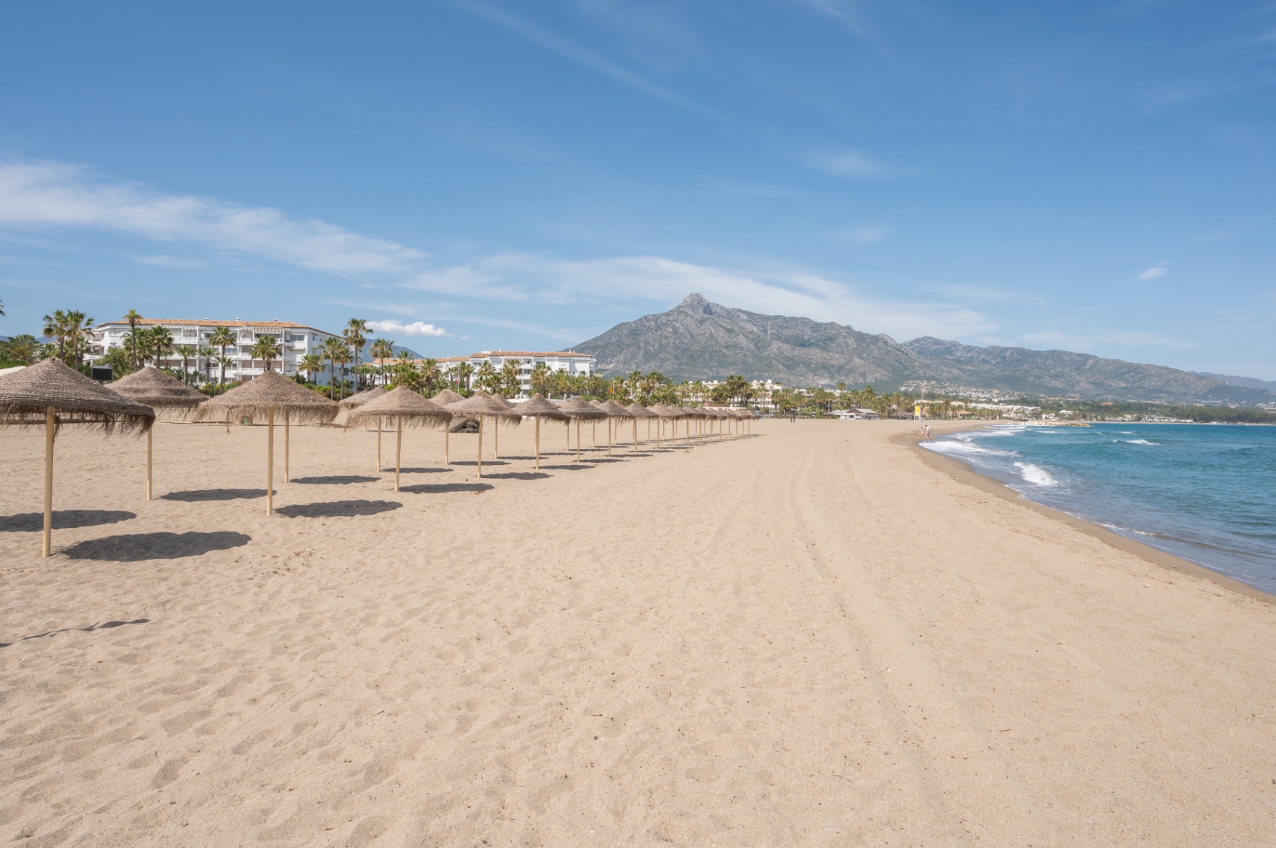Empty Marbella beach with thatched parasols and La Concha behind.